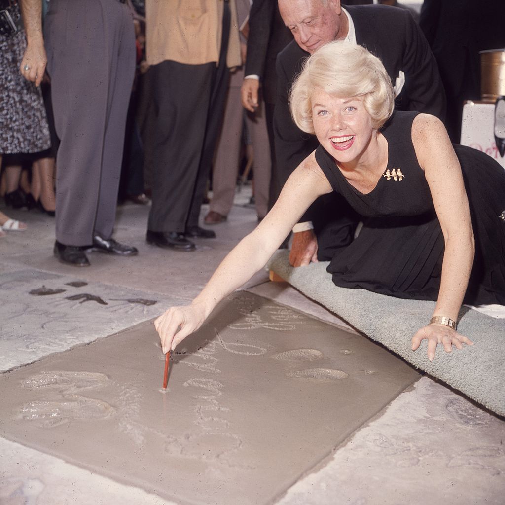 Image Credits: Getty Images / Hulton Archive | American singer and actress Doris Day smiling as she signs her name in cement by her handprints, in front of Mann's (formerly Grauman's) Chinese Theater, on Hollywood Boulevard, Hollywood, California.