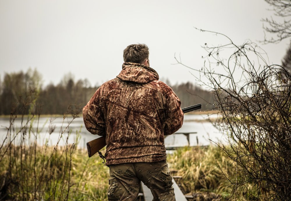 Hunter with a gun tracks down ducks on the river. | Shutterstock Hunter with a gun tracks down ducks on the river. | Shutterstock