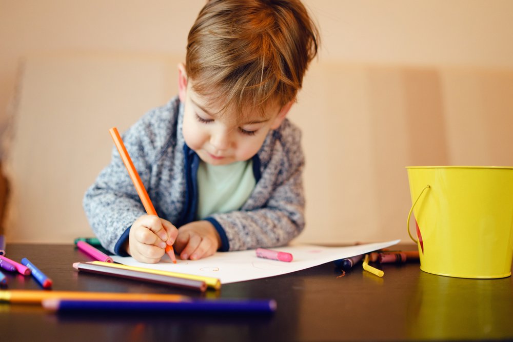Young boy plays with crayons at table | Shutterstock
