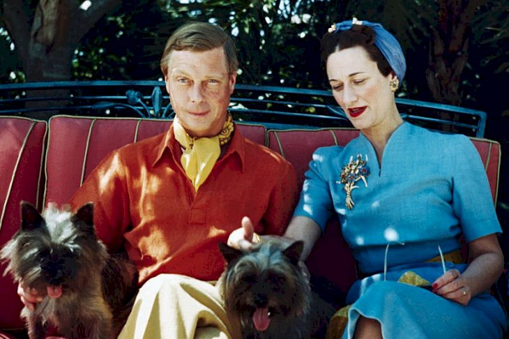 Image Credits: Getty Images / Bettmann | The Duke and Duchess of Windsor seated outdoors with two small dogs.