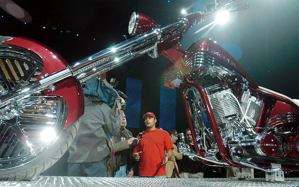 Image Credits: Getty Images / Bryan Mitchell | Paul "Paulie" Teutul Jr. and his father Paul Sr. from Orange County Choppers and the television show American Chopper talks to the automotive press about the Lincoln Mark LT Chopper they built January 10, 2005 at the North American International Auto Show in Detroit, Michigan.