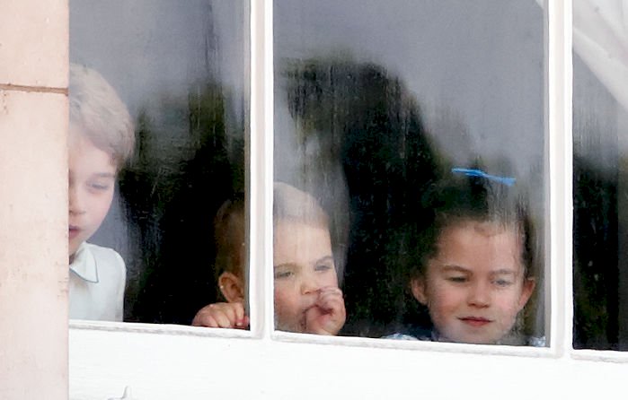 Image Credit: Getty Images / Prince George of Cambridge, Prince Louis of Cambridge (sucking his thumb) and Princess Charlotte of Cambridge look out of a window of Buckingham Palace.