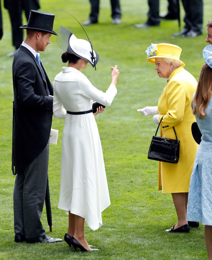 Image Credits: Getty Images | The Queen is photographed speaking with Meghan Markle and Prince Harry.