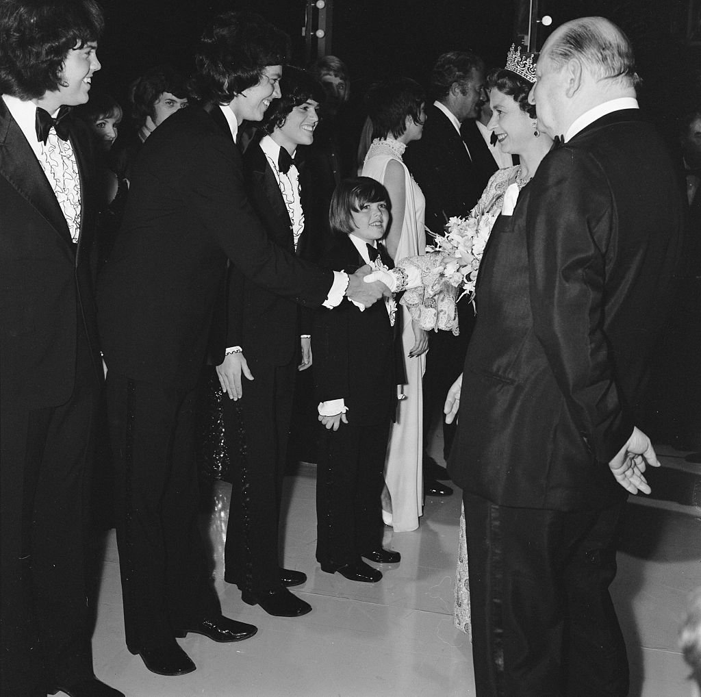 Image Source: Getty Images/MirrorpixHer Majesty Queen Elizabeth II, escorted by Media mogul Lew Grade (right), shakes hands with a member of the Osmonds pop