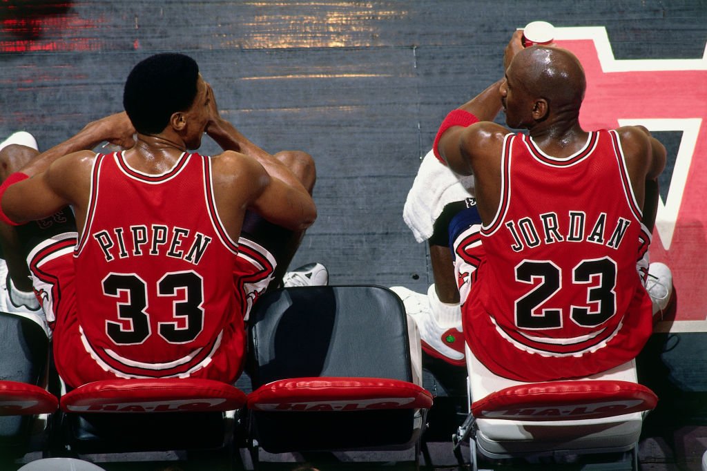Image Credits: Getty Images / Andy Hayt / NBAE | Scottie Pippen #33 and Michael Jordan #23 of the Chicago Bulls sit on the bench during the game against the Vancouver Grizzlies at General Motors Place on January 27, 1998 in Vancouver, British Columbia, Canada.