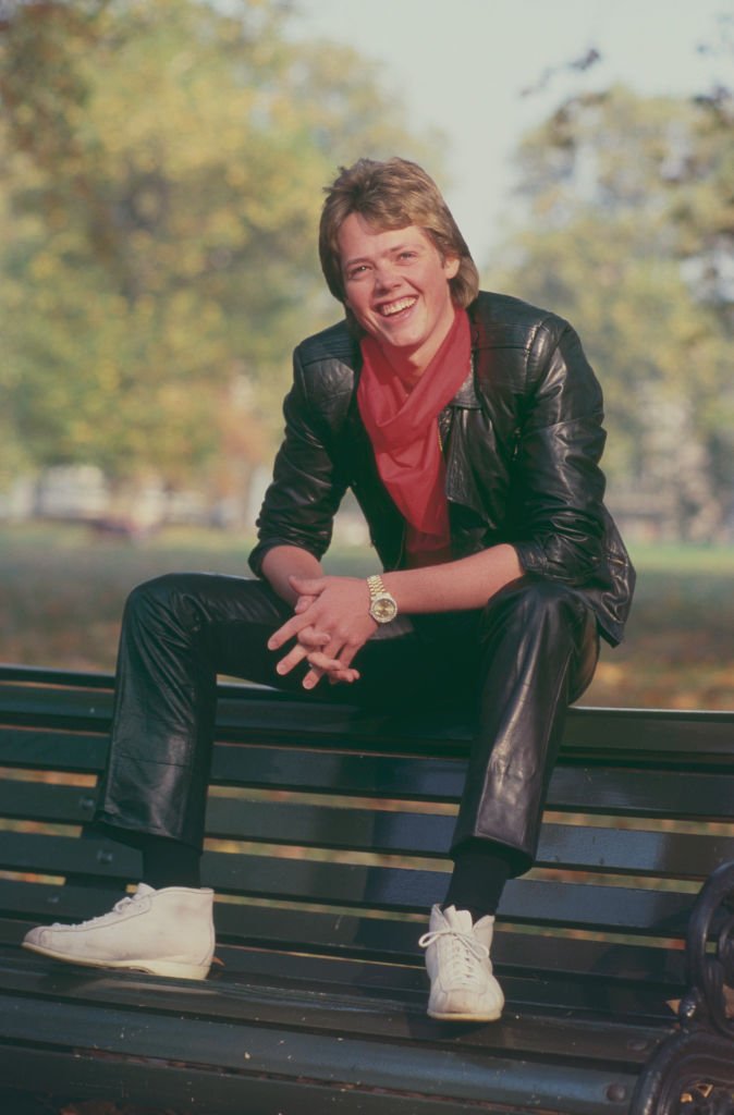 Image Credits: Getty Images / Michael Putland | Jimmy Osmond, American singer and member of American family group The Osmonds, posed wearing a leather jacket and trousers as he sits on a bench in a park in London in October 1983.