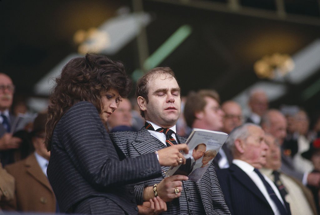 Image Credit: Getty Images / Elton John singing the Cup Final Hymn with his wife Renate Blauel at Wembley Stadium before the FA Cup Final in 1984.