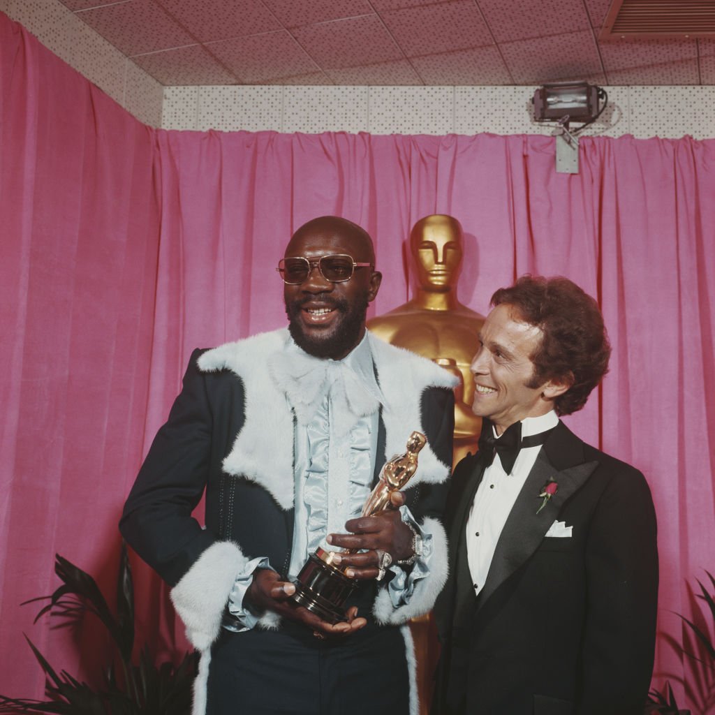 Image Credits: Getty Images / Rolls Press/Popperfoto | American musician and actor Isaac Hayes pictured holding his Oscar statuette Academy Award with actor Joel Grey