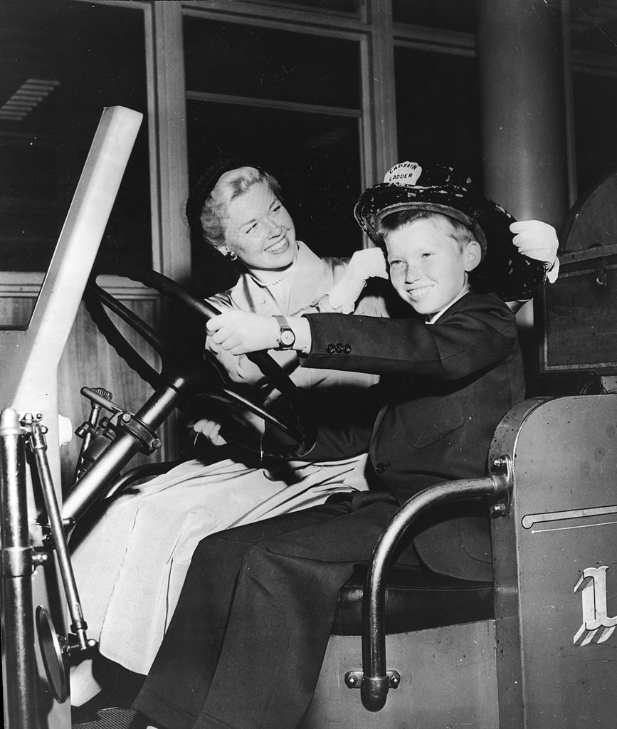 Image Credits: Getty Images / Hulton Archive | American actor and singer Doris Day smiling as she sits next to her son, Terry, in a fire truck, Cincinnati, Ohio. Day was visiting relatives in her hometown of Cincinnati while promoting the film 'By the Light of the Silvery Moon.'
