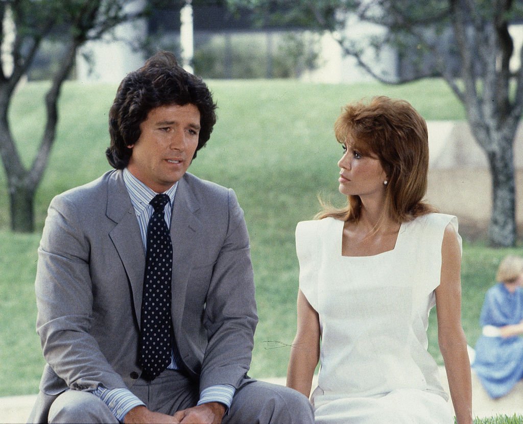 Image Credit: Getty Images / In a scene from the American television series 'Dallas,' American actors Patrick Duffy (as Bobby Ewing) and Victoria Principal (as Pamela Barnes Ewing) sit outside.