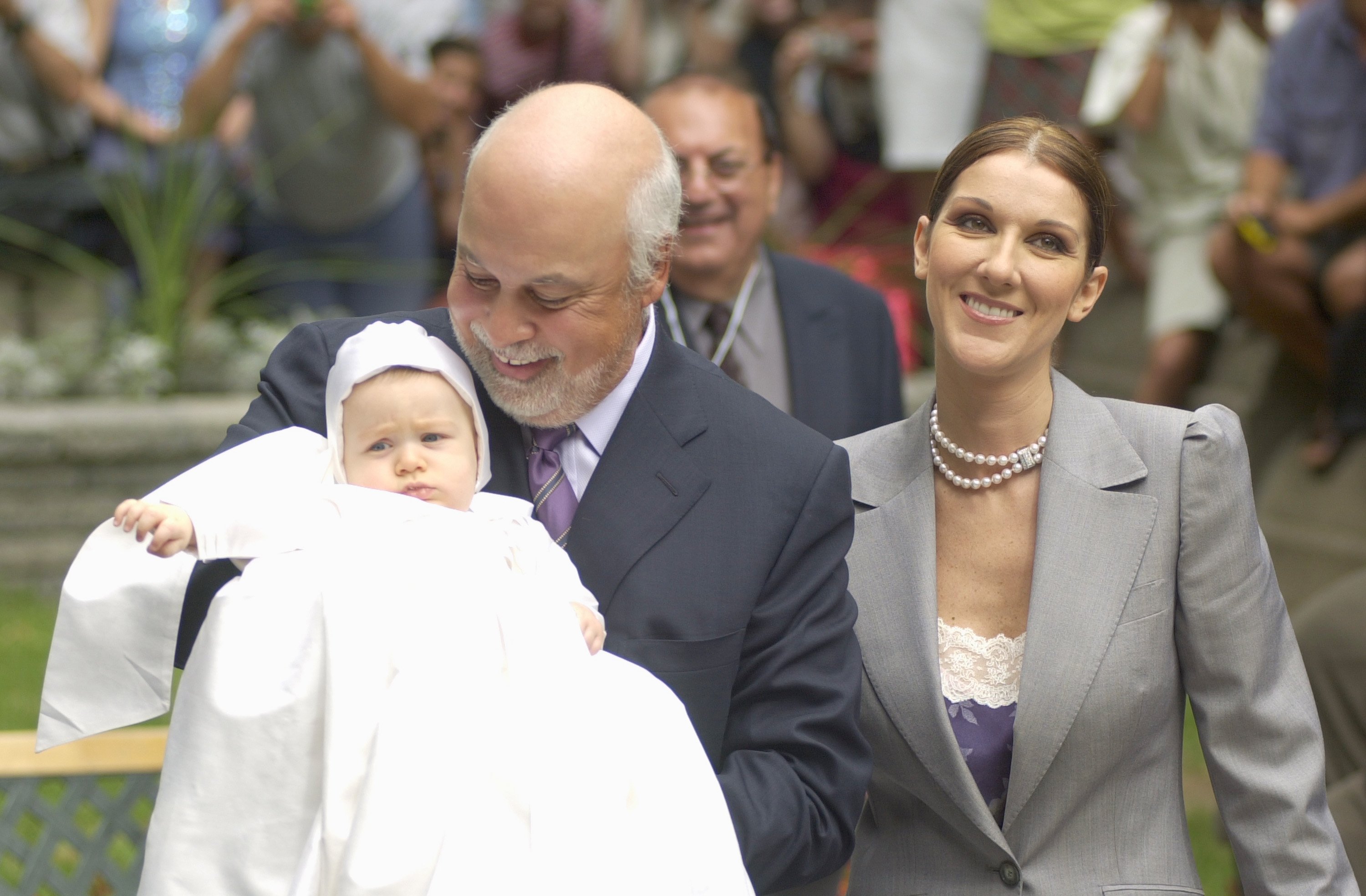 Image Credits: Getty Images / Pierre Roussel | Pop star Celine Dion stands next to her husband, Rene Angelil, who holds their baby Rene-Charles July 25, 2001 as they arrive at the chapel of the Notre-Dame Basilica in old Montreal, Quebec before the baptism of their 6-month-old baby boy.