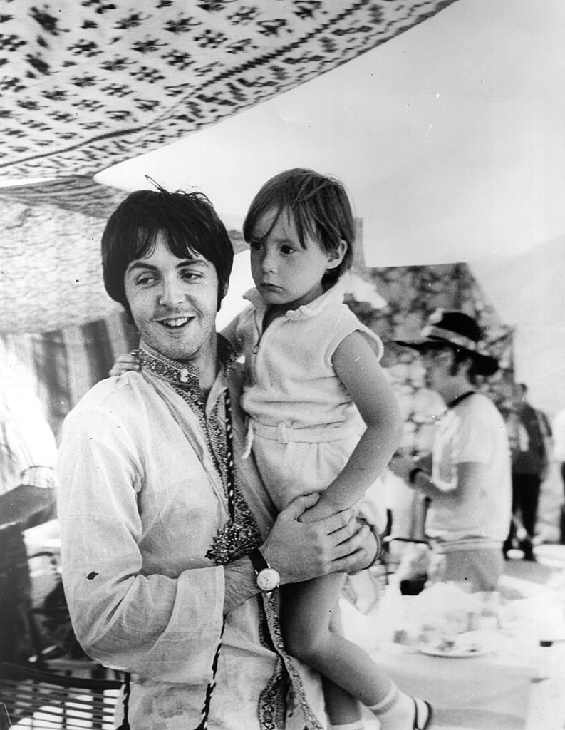 Image Credits: Getty Images / Central Press | Beatles singer and bass player Paul McCartney holds four year old Julian, son of his colleague John Lennon (visible in the background) during a holiday near Athens in Greece.